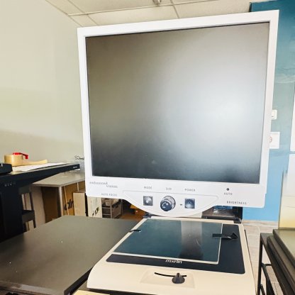large monitor with three black tactile large buttons on bottom. Under the monitor is a built in table
