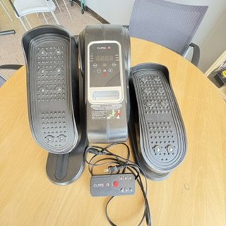 black mini stepper machine with display in the middle, wires and remote control on bottom of picture